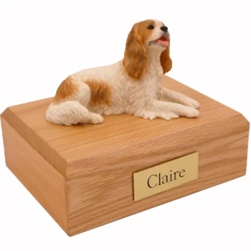 Laying brown and white King Charles Spaniel dog figurine on wood memorial cremation urn