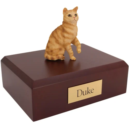 Sitting red shorthair tabby cat figurine on wood cremation urn