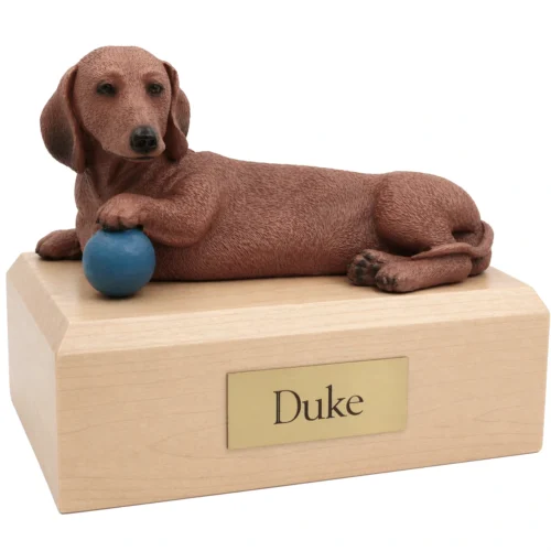 Memorial cremation urn with laying brown Dachshund with blue ball dog figurine, maple finish